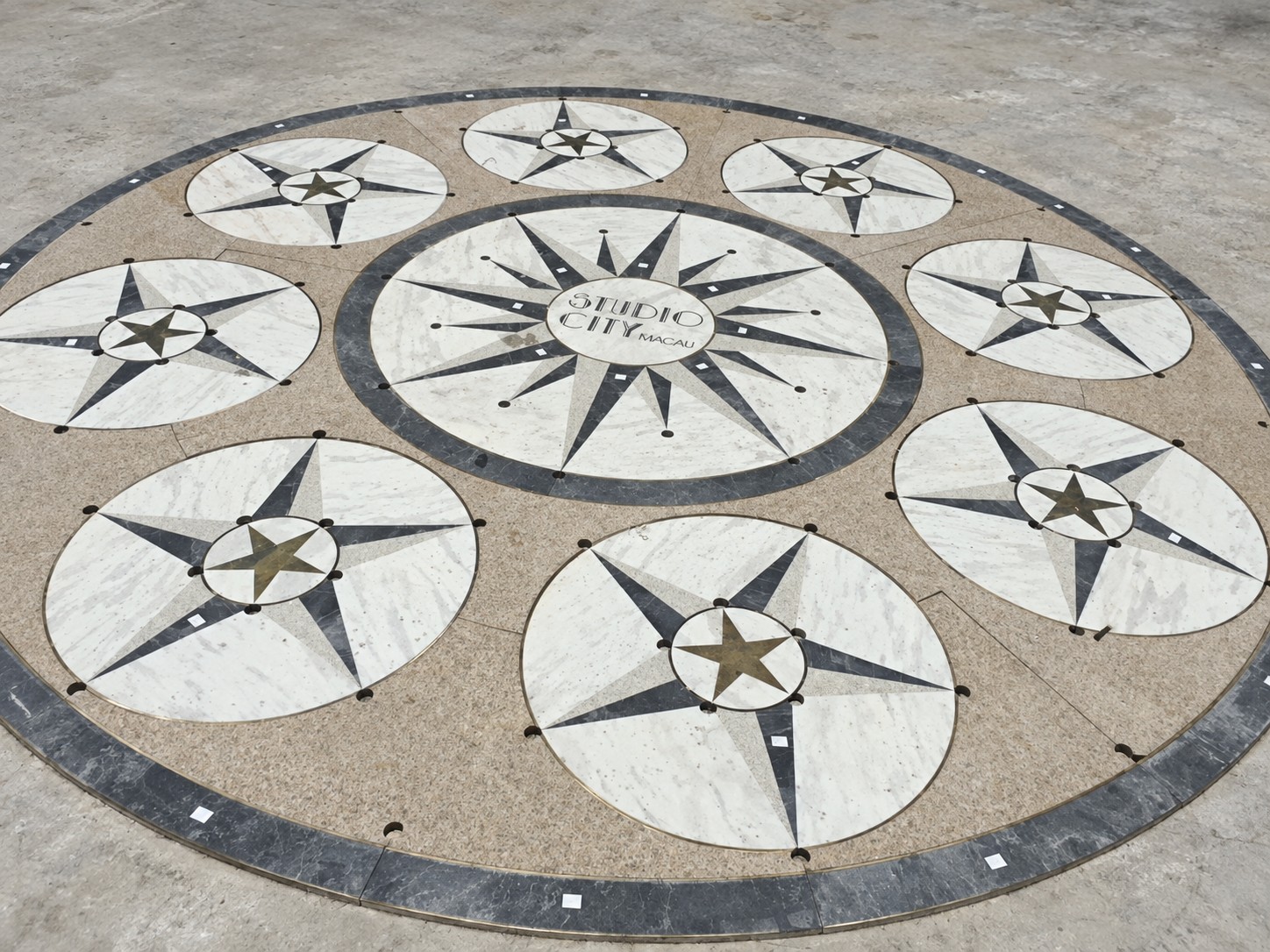 A ten-medallion compass floor for Studio City, Macau, with a large central starburst medallion reading STUDIO CITY MACAU, in marble and dark stone with brass star and dot insets