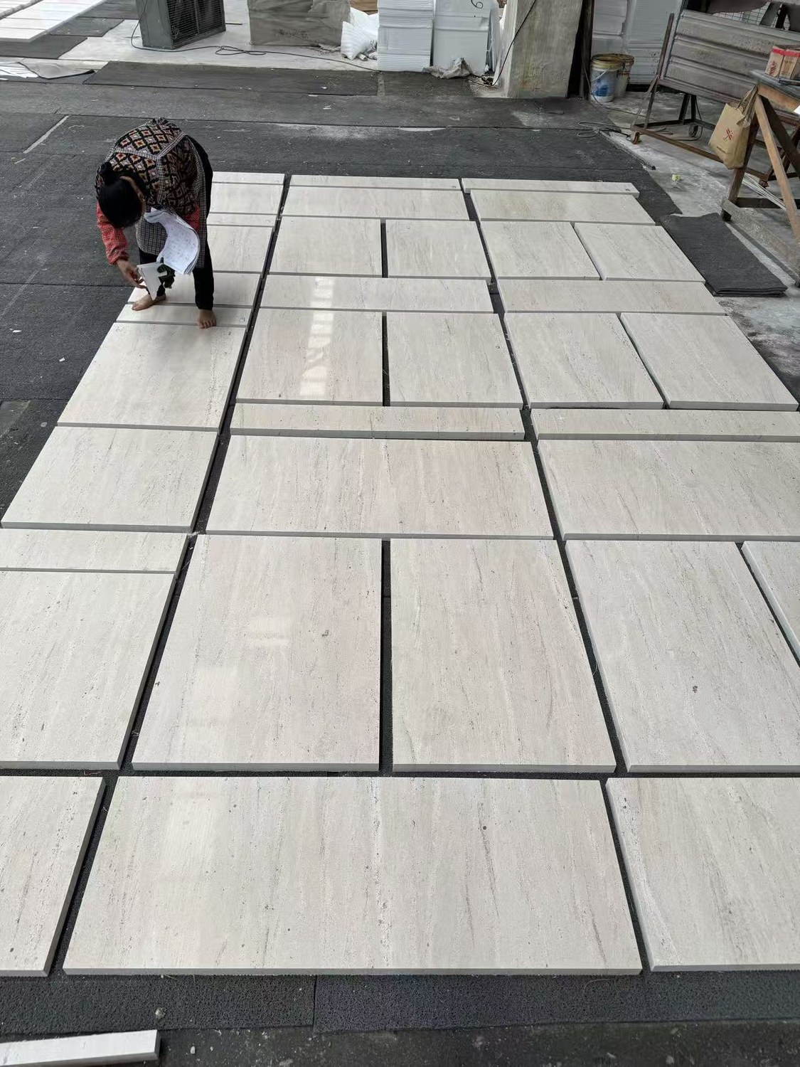 A worker checking an Ivory Travertine floor layout against a reference sheet before packing