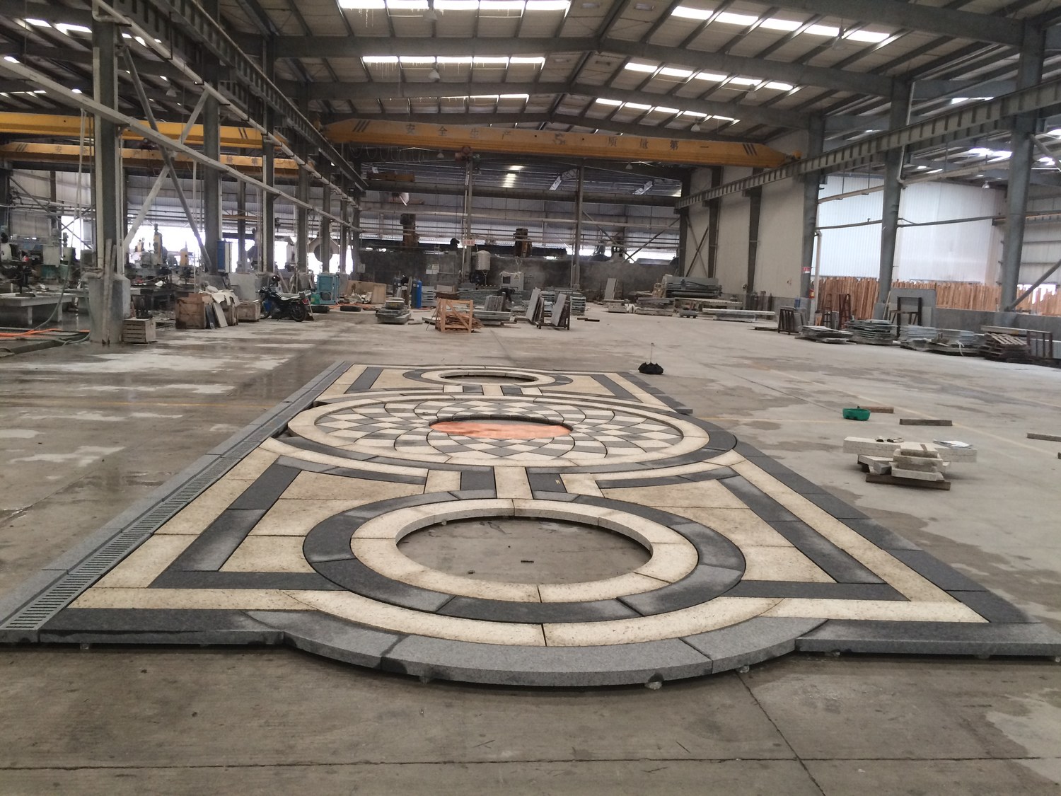 A granite paving medallion dry-laid on the factory floor, with production machinery visible in the background