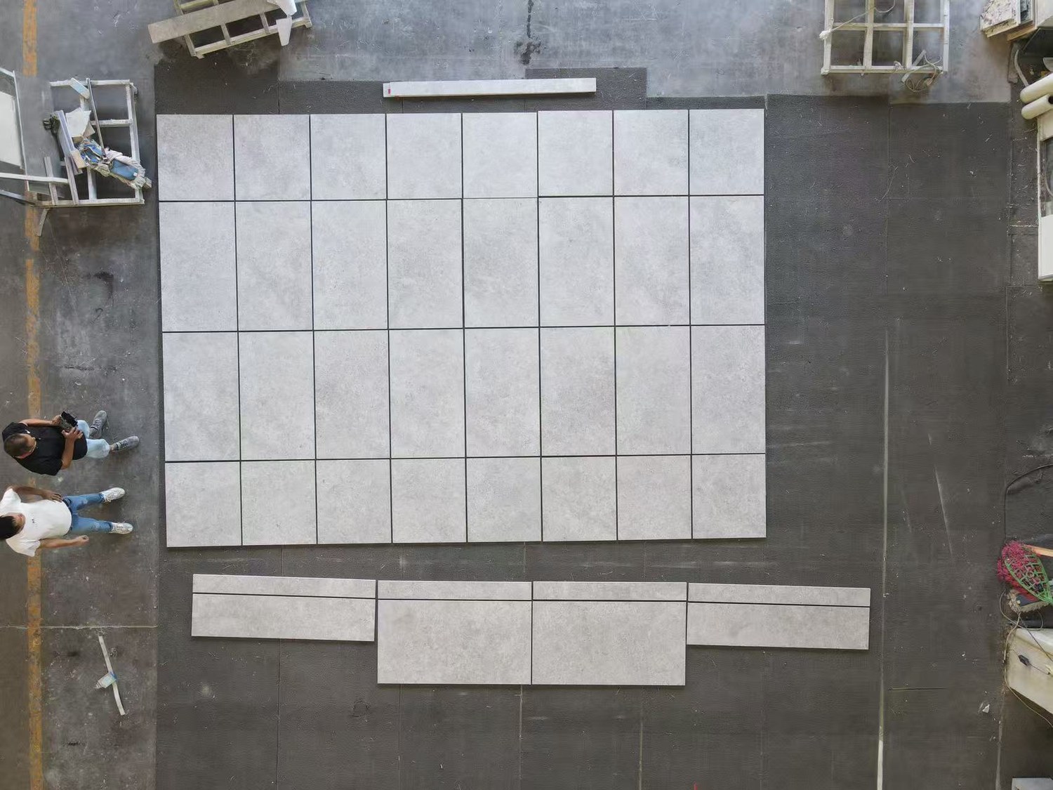 An aerial view of light grey Moca Grey Limestone tiles with cloud-like mottling, laid out on a factory floor with narrower cut border pieces below