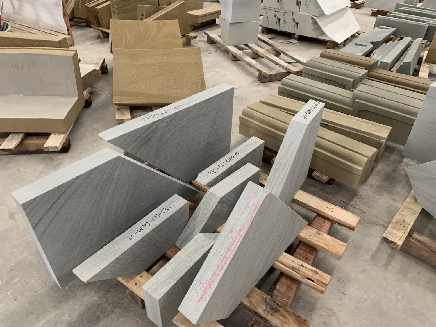 Cut sandstone pieces on pallets, each marked with a handwritten reference code