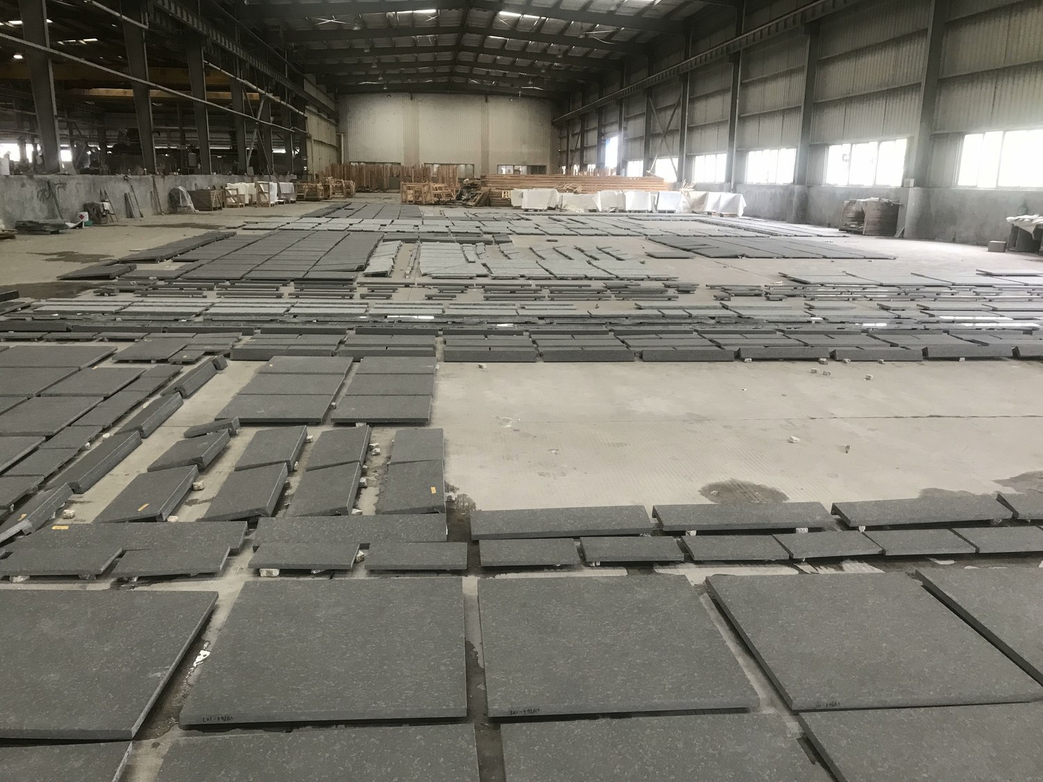 Hundreds of finished dark stone paving pieces laid out across a factory floor for final inspection
