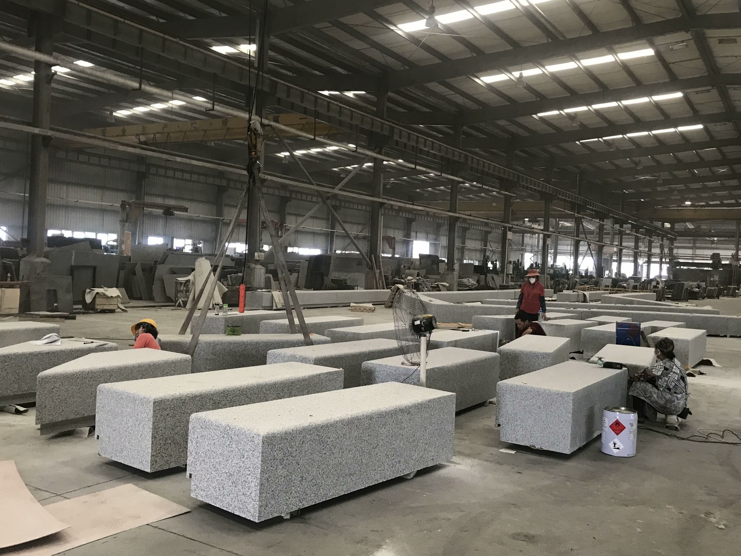 Rows of Wuhan G603 grey granite paving units being finished by workers in a factory