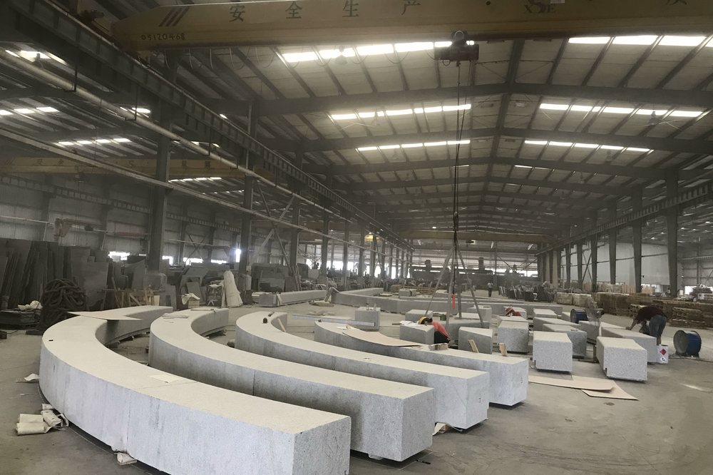 Curved grey granite benches and site elements in production on the factory floor