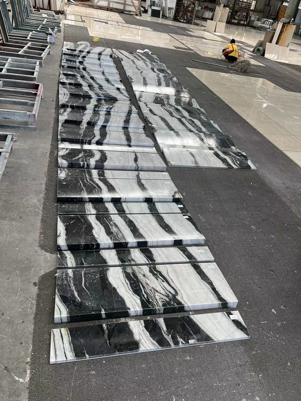 A long run of cut marble pieces with continuous veining laid out across a factory floor