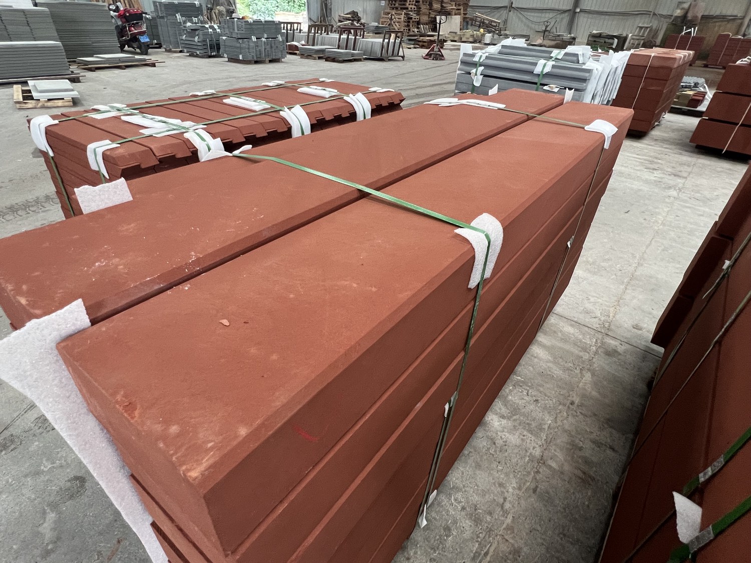 Large red sandstone kerb and coping units with a grooved anti-slip profile, strapped and packed for shipping in a factory yard