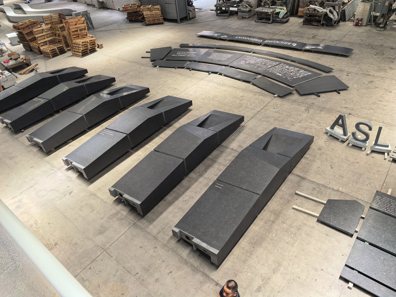 The complete set of a public memorial's curved signage, engraved benches and lettering, staged together in a factory before shipment