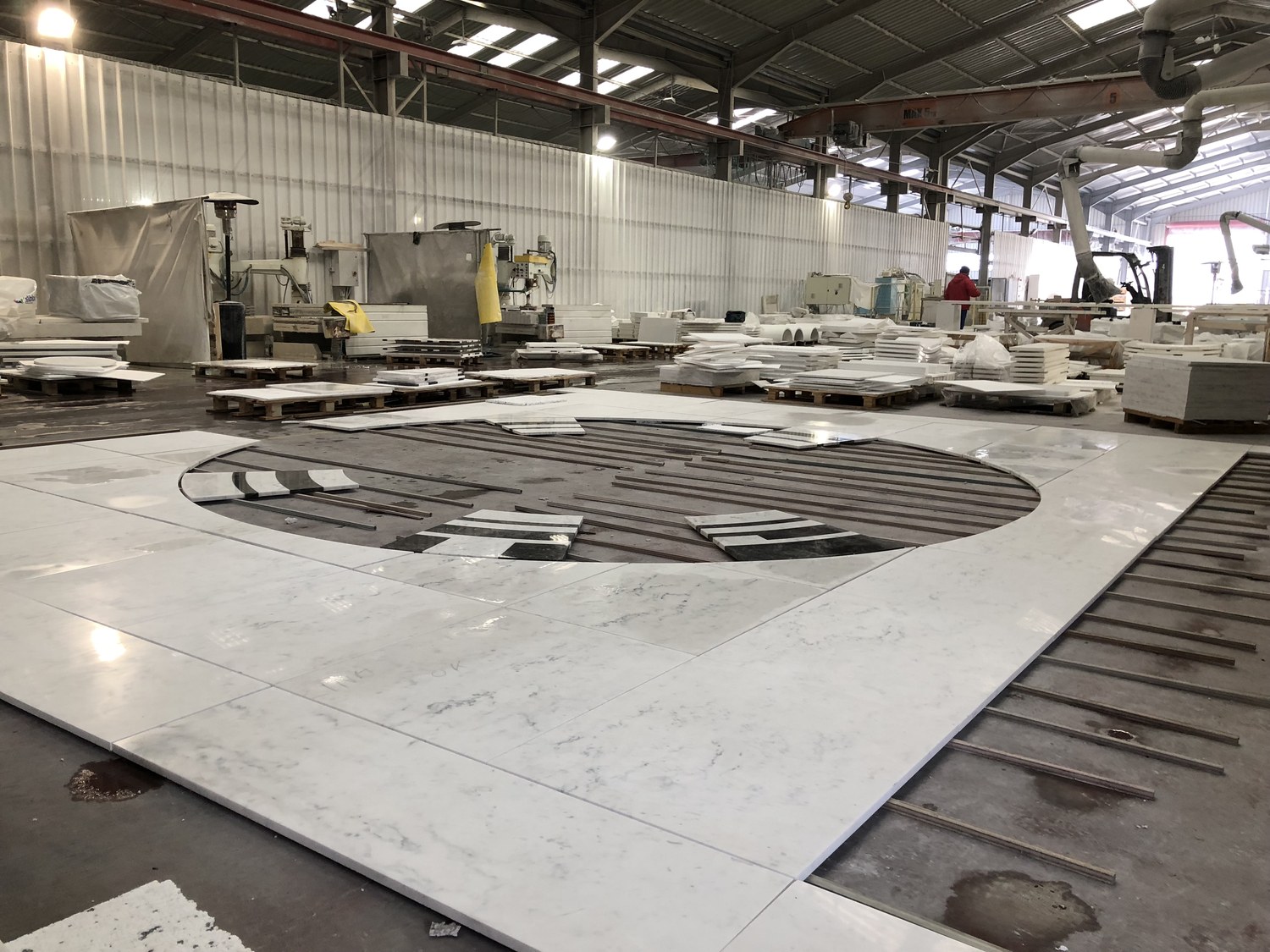 Workers checking a large circular marble medallion pattern assembled on a factory floor