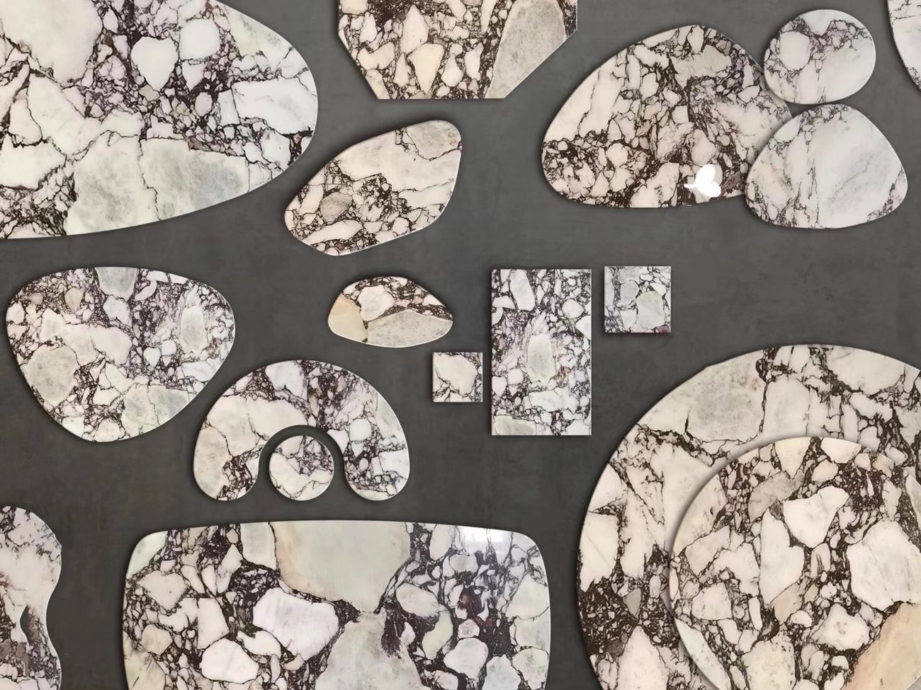 Violet-veined marble cut into organic shapes and rounds for furniture tops, laid out for inspection